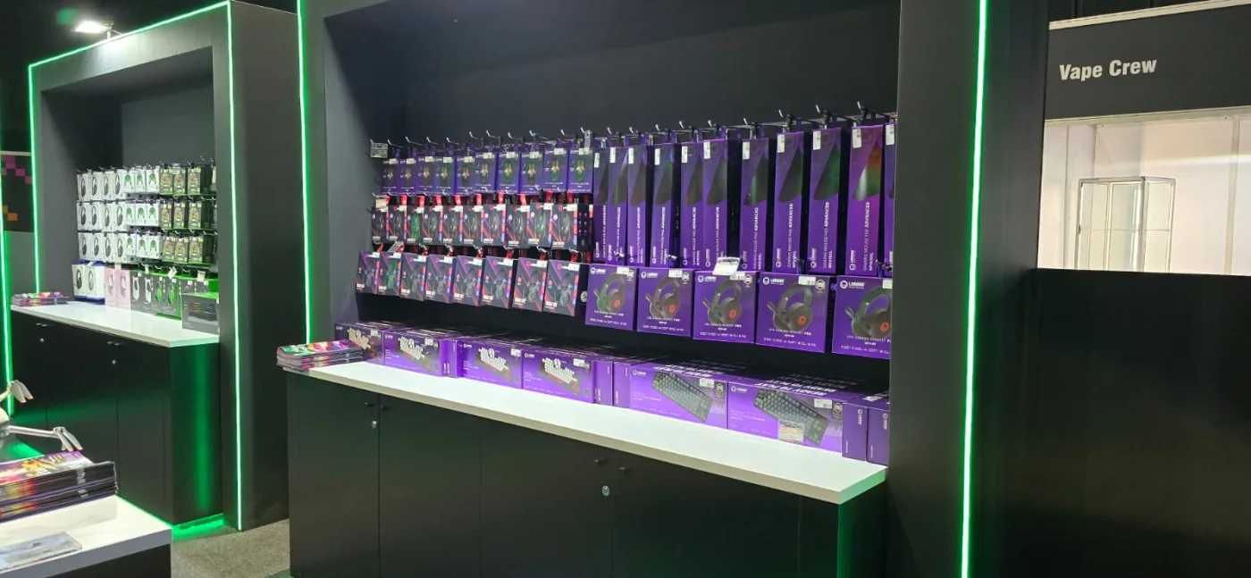 The LORGAR retail display: shelves of boxed headsets, mice, mouse pads and keyboards in LORGAR purple packaging, under green strip lighting.
